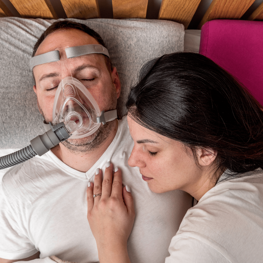 wife-laying-on-husband-who-is-wearing-a-sleep-apnea-mask